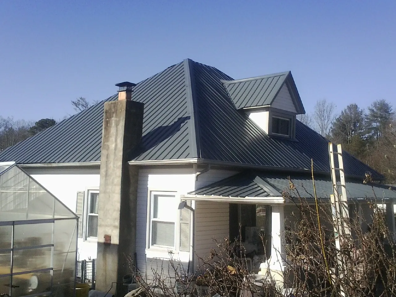Dark blue standing seam metal roof on a white farmhouse with dormer — Slate & Tile Roof Repair by Roofing Brothers in Hallsville