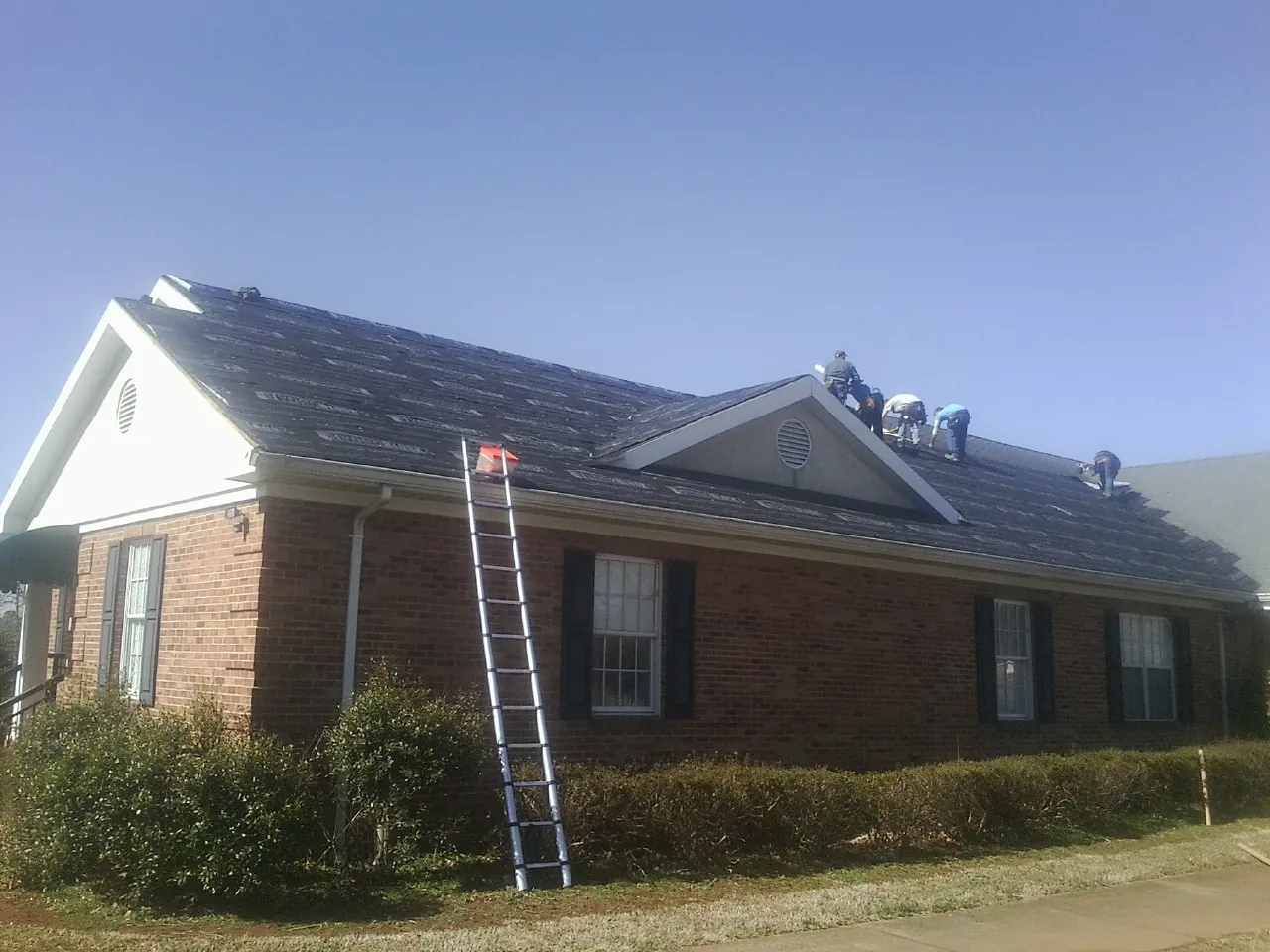 Crew tearing shingles off a brick ranch roof with a ladder set — Metal Roof Repair work by our crew in Hallsville