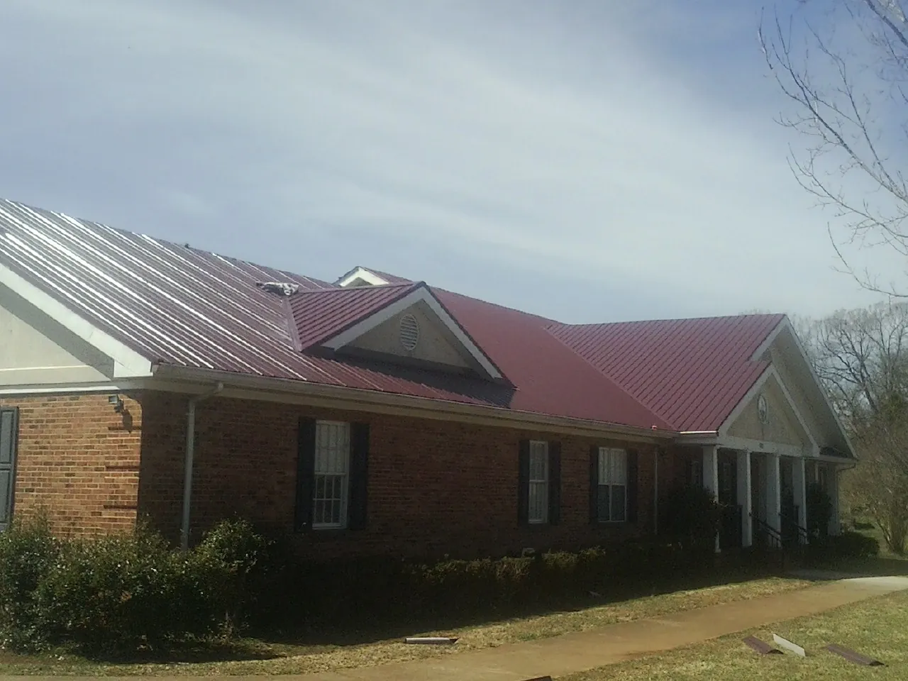 Red metal roof with gabled entries on a long brick building, from a Hail Damage Roof Repair job in Hallsville