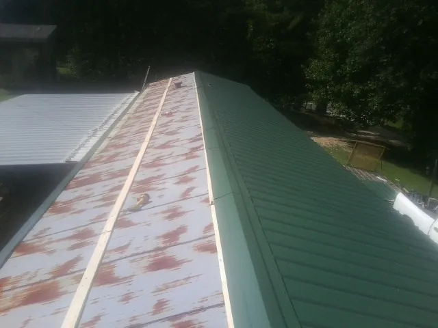 Old rusted panels beside newly installed green metal roofing — Wind Damage Roof Repair by Roofing Brothers in Hallsville
