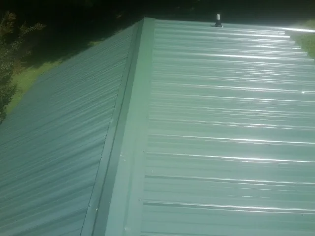 New green metal panels meeting at the ridge of a roof — Flat Roof Repair work by our crew in Hallsville