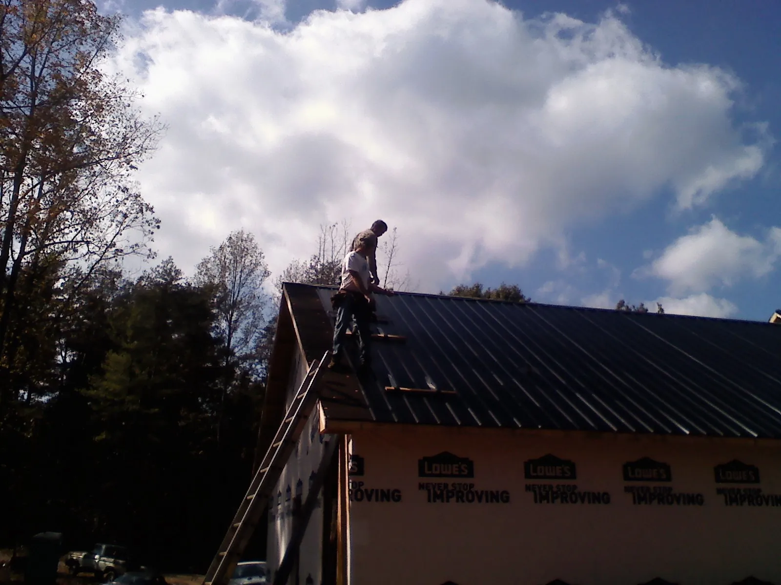 Roofer fastening dark metal panels high against a cloudy sky, from a Roof Inspection job in Hallsville