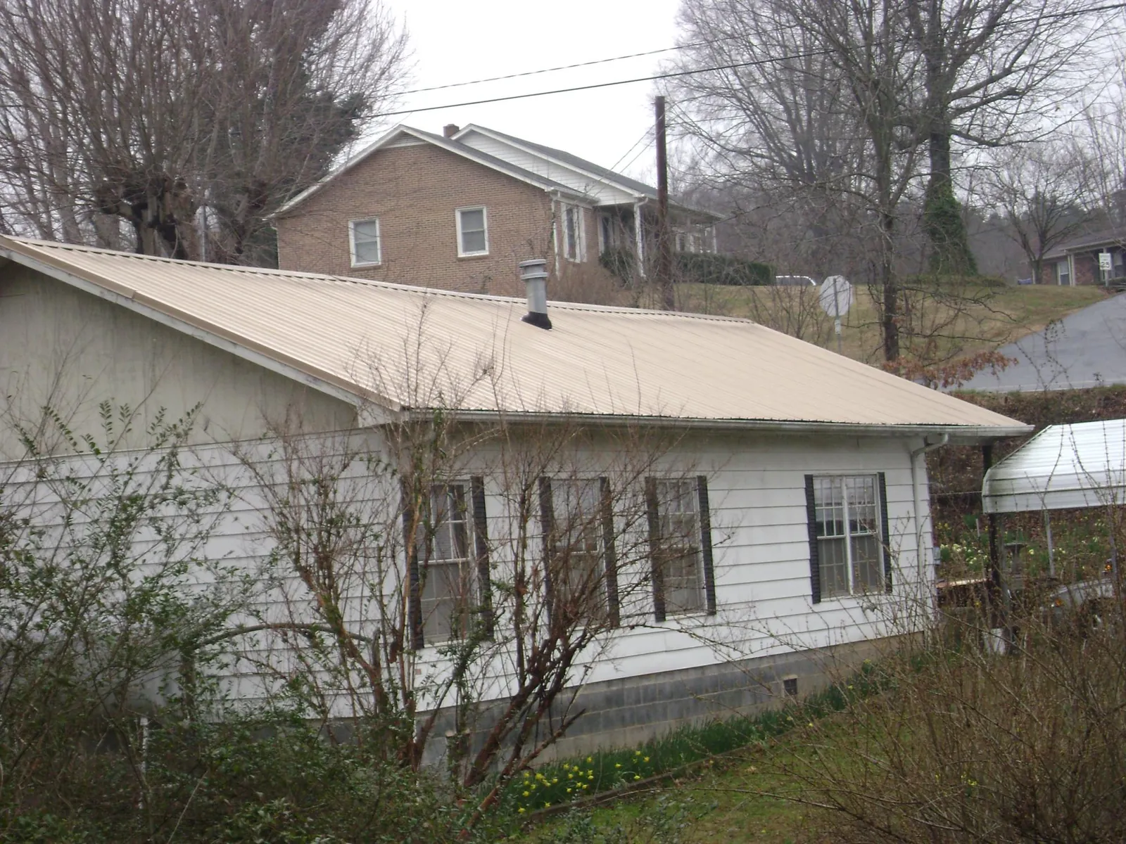 Tan metal roof on a white sided house set into a hillside — Commercial Roofing by Roofing Brothers in Hallsville