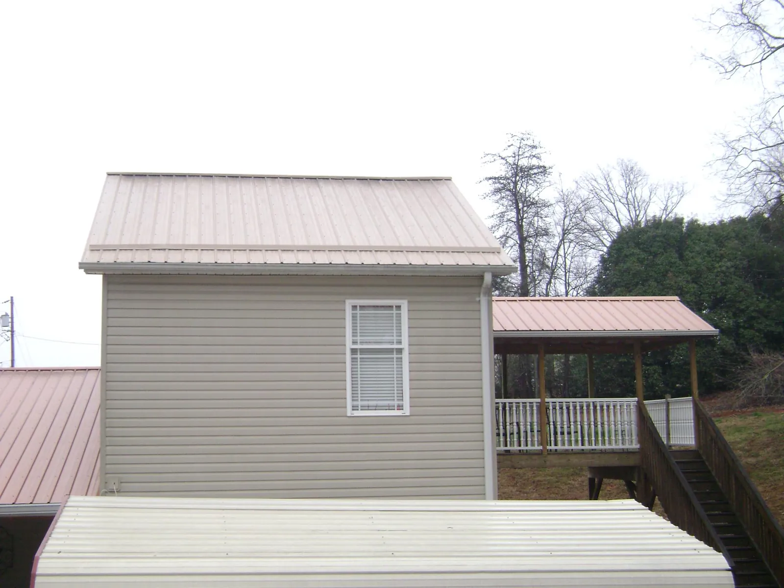Tan metal roofs on a two story addition and attached porch, from a Roof Replacement job in Hallsville